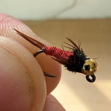 A Copper John held between two fingers: red wire body, gold bead.
